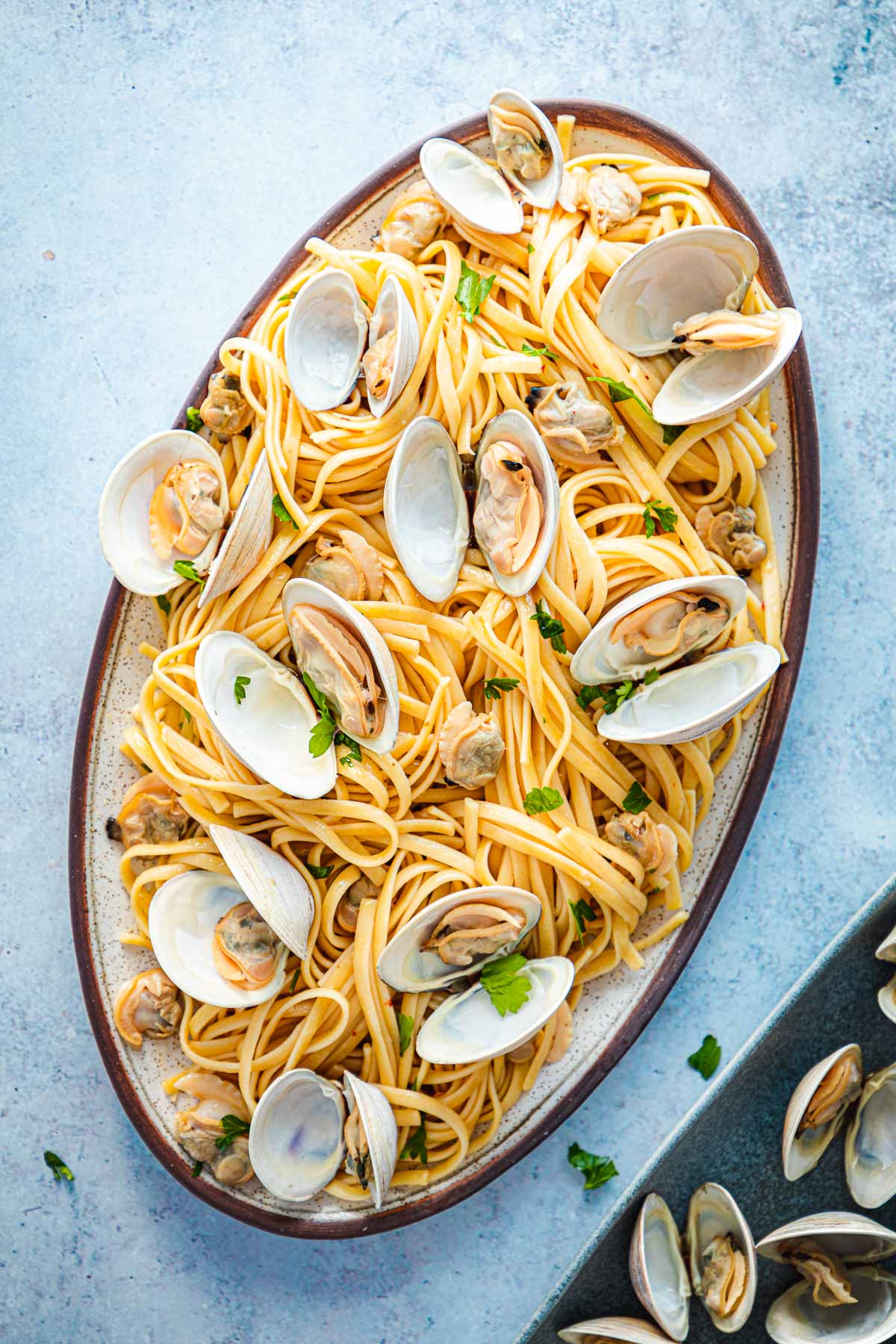 Large serving of linguini with clams in an oblong, shallow serving bowl with a brown rim.