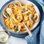 Side shot of a serving of linguini with clams with a blue linen napkin on the side.