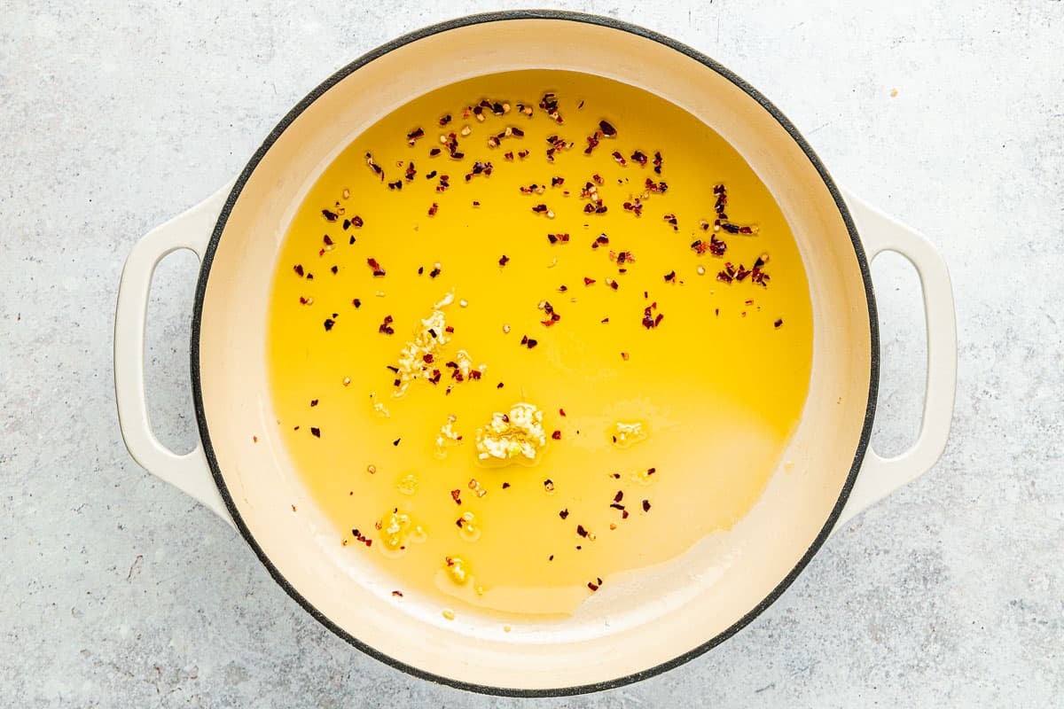 Garlic and red pepper flakes that have just been added to a pot of oil.