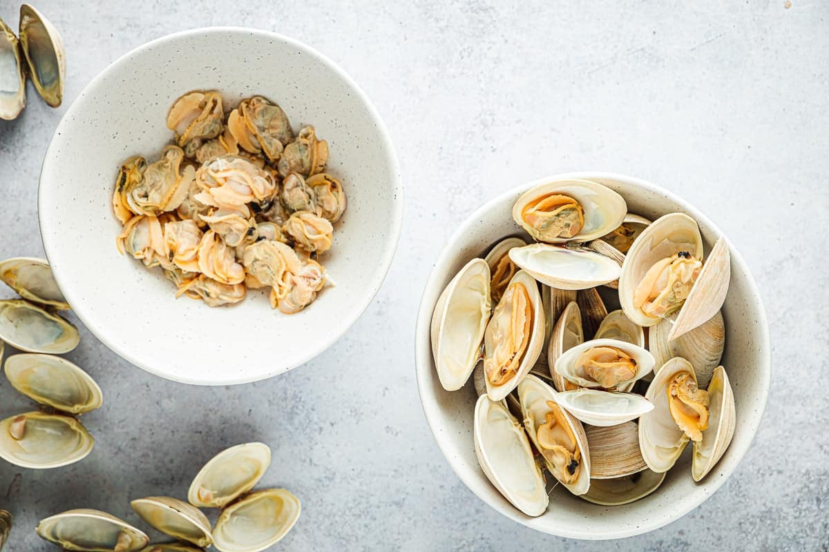 Overhead shot of two bowls, one with clams in their shell, one with just clam meat.