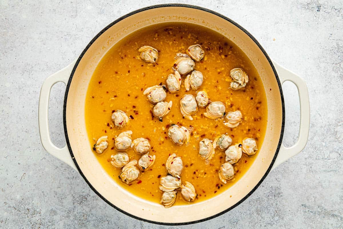 Overhead shot of shucked clams in a pot with their juice, garlic, red pepper flakes, and white wine.