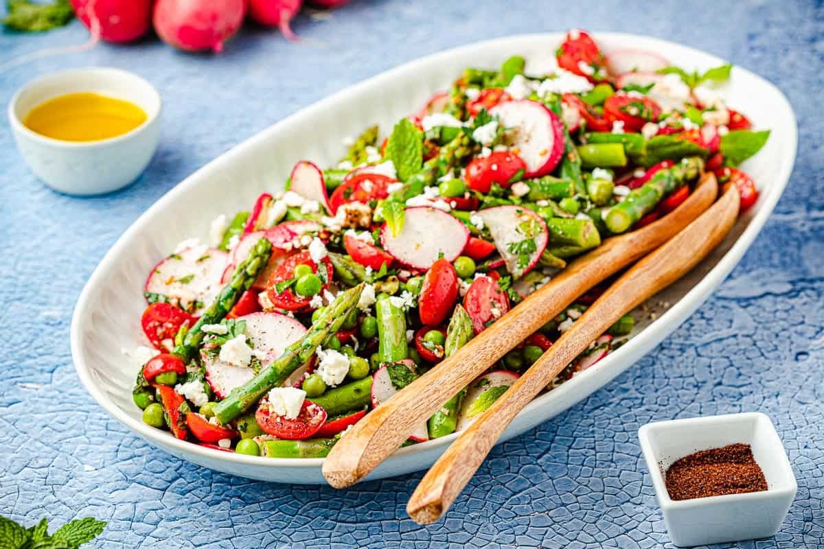 Asparagus salad with wooden serving spoons and dressing and sumac on the side.