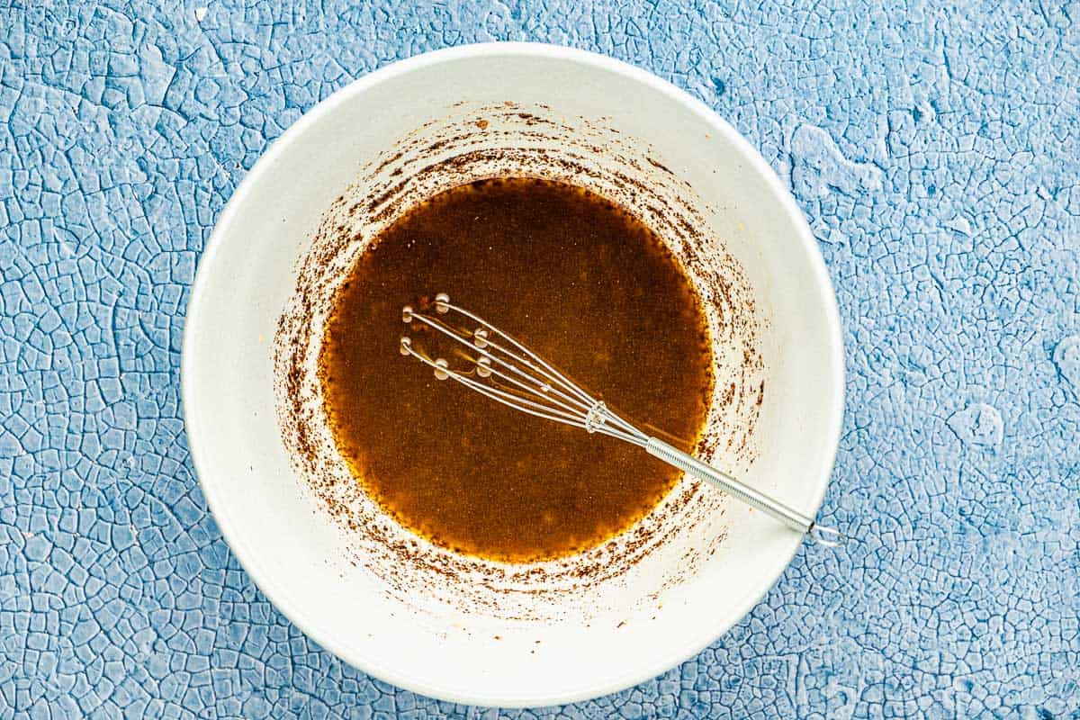 Vinegar, garlic, a big pinch of salt and pepper, and sumac, and a whisk in a white bowl.