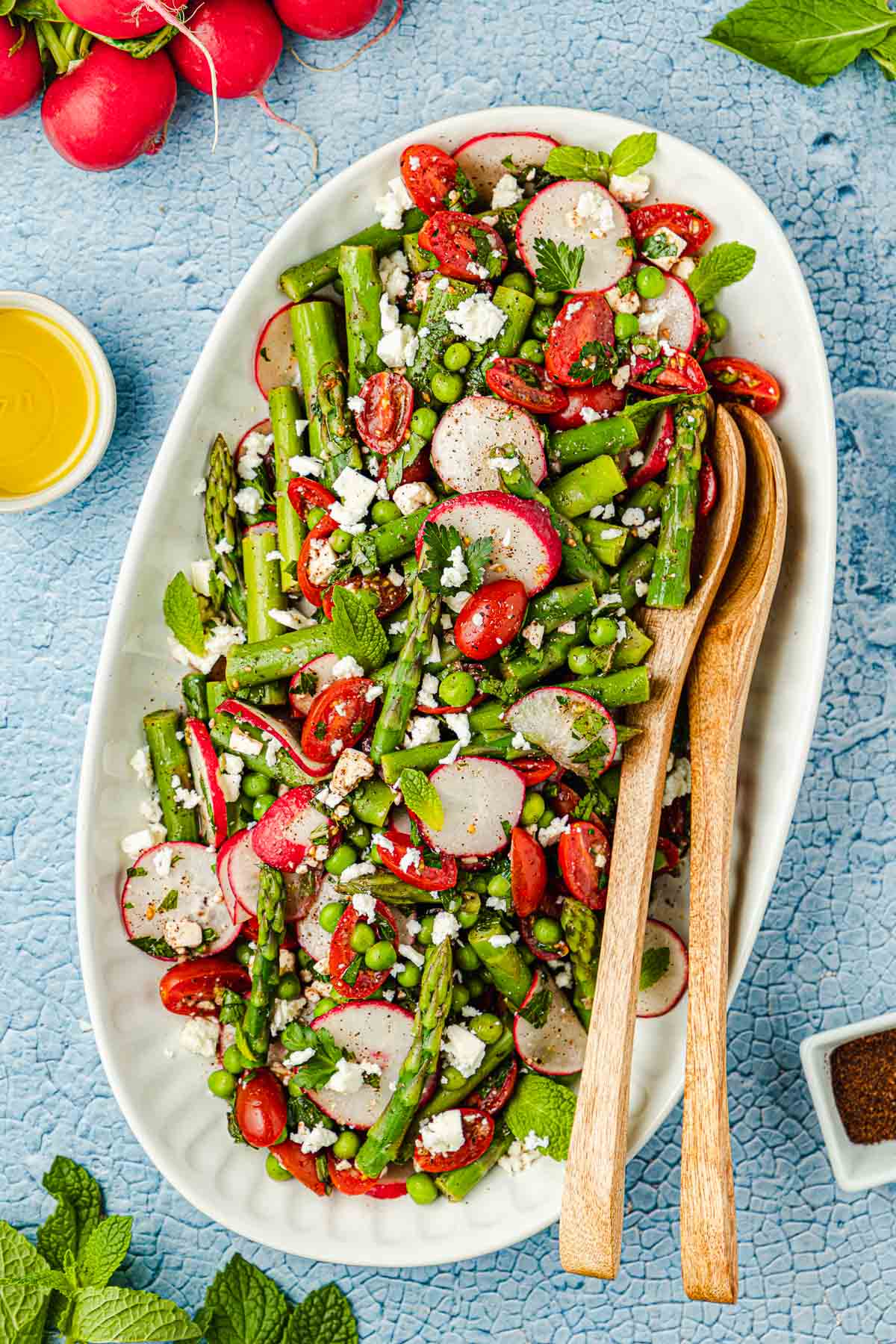 Asparagus salad on a large white serving platter with two wooden serving spoons.