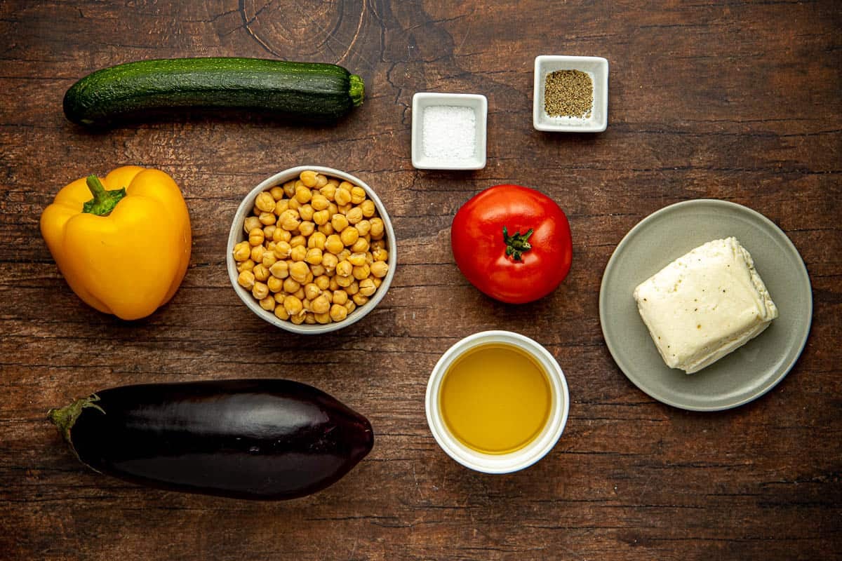 Ingredients for Roasted Vegetable Salad with Halloumi, including tomato, salt, pepper, zucchini, chickpeas, bell pepper, eggplant, oil, and halloumi cheese.
