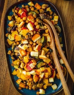 Overhead shot of Roasted Vegetable Salad on a blue serving dish with two wooden serving spoons.