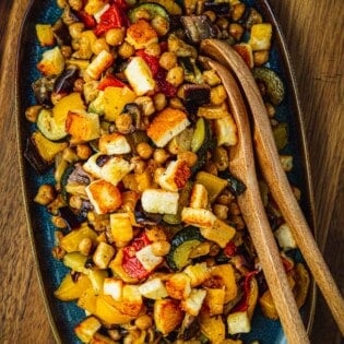 Overhead shot of Roasted Vegetable Salad on a blue serving dish with two wooden serving spoons.