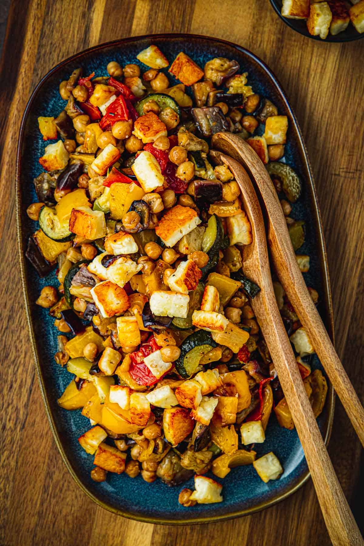 Overhead shot of Roasted Vegetable Salad on a blue serving dish with two wooden serving spoons.