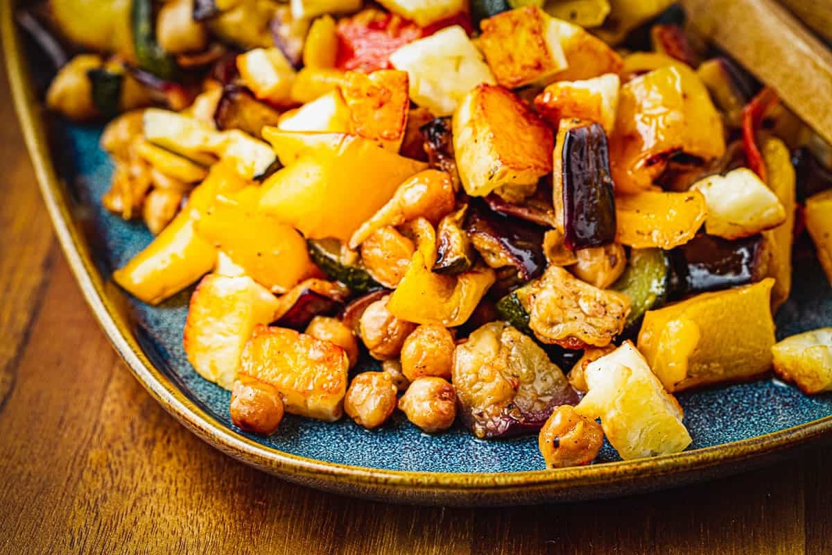 Side shot closeup of roasted eggplant, chickpeas, zucchini, tomato, and bell pepper.