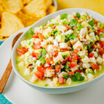 a bowl of shrimp ceviche on a plate with a wooden spoon with a bowl of tortilla chips in the background.