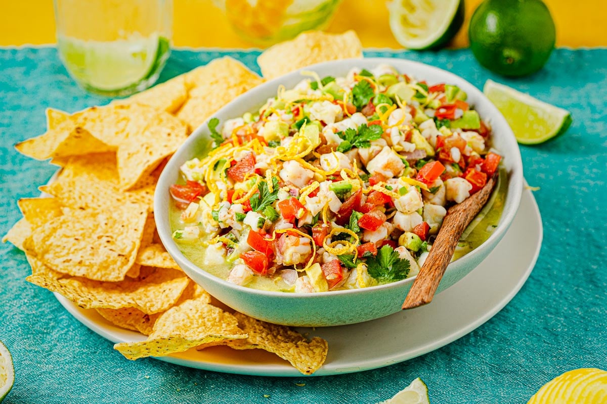 a bowl of shrimp ceviche with a wooden spoon on a plate of tortilla chips.