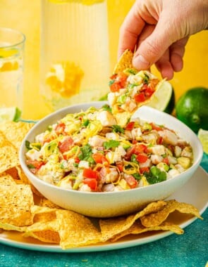 a hand lifting shrimp ceviche on a tortilla chip from a bowl of ceviche.