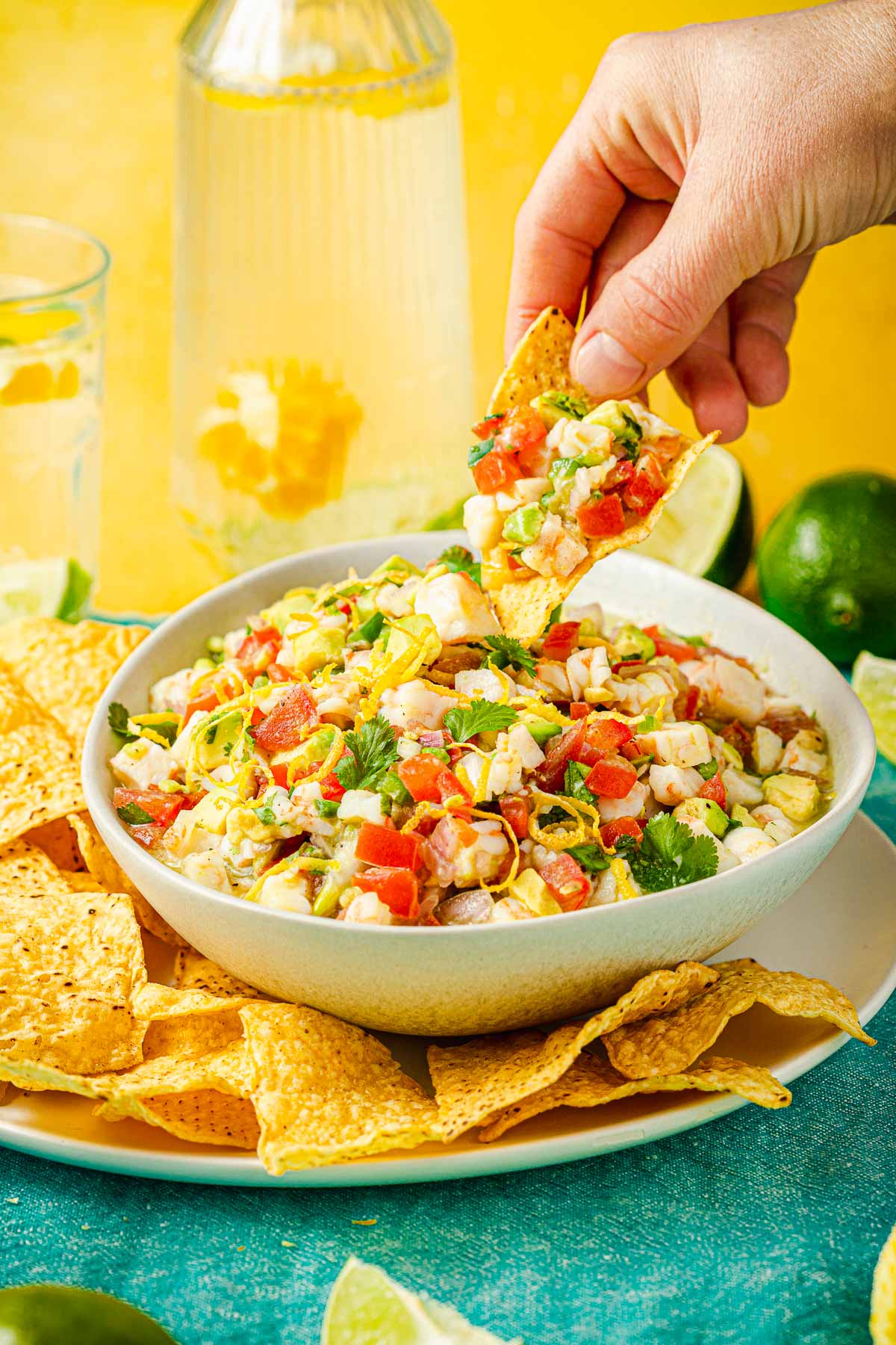 a hand lifting shrimp ceviche on a tortilla chip from a bowl of ceviche.