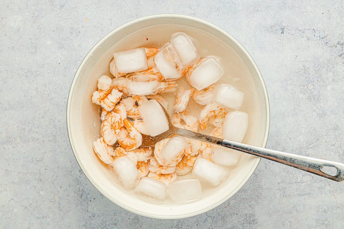 cooked shrimp in a bowl of ice water with a spoon.