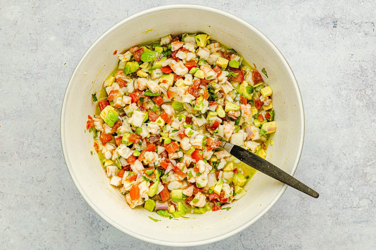 shrimp ceviche being mixed in a bowl with a spoon.