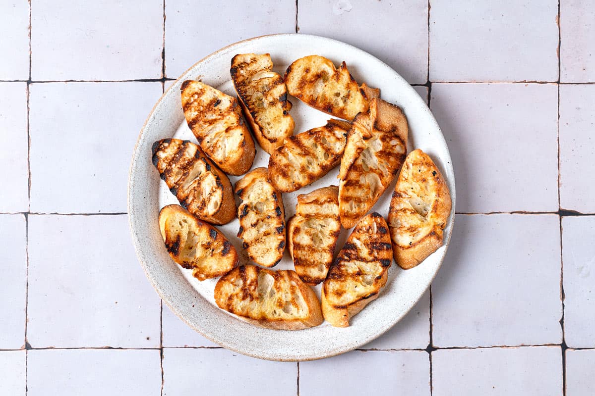 Sliced baguette that has been grilled and placed on a white plate.