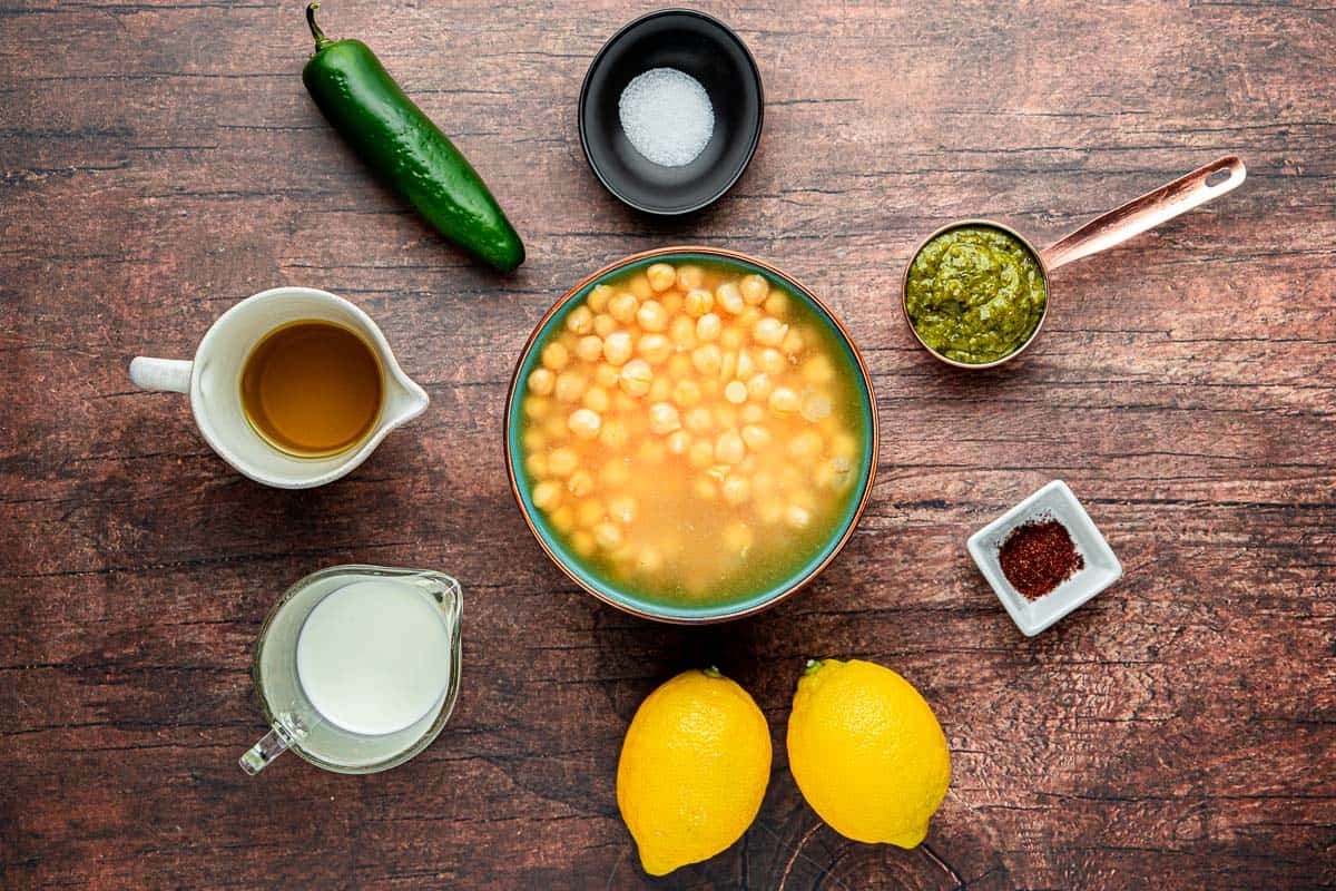 ingredients for creamy pesto braised chickpeas including chickpeas, olive oil, salt, lemons, basil pesto, cream, jalapeno, and sumac.