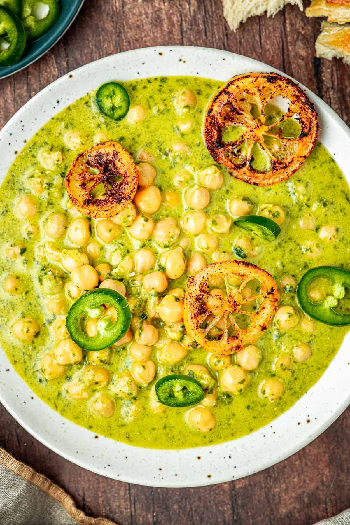 a clost up of a bowl of creamy pesto braised chickpeas topped with sliced jalapenos and fried lemon rings.