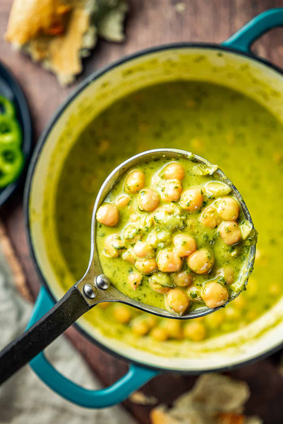 creamy basil pesto chickpeas being scooped out of a pot with a ladle.