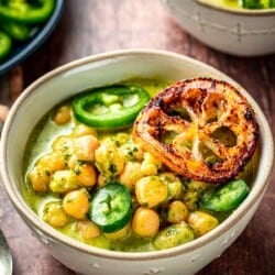 gros plan de deux bols de pois chiches braisés au pesto crémeux garnis de jalapeno et de tranches de citron frites, à côté d'une assiette de tranches de jalapeno.