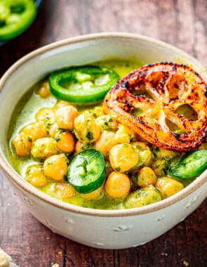 close up of two bowls of creamy pesto braised chickpeas topped with jalapeno and fried lemon slices next to a plate of sliced jalapenos.