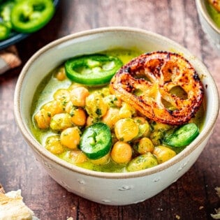 close up of two bowls of creamy pesto braised chickpeas topped with jalapeno and fried lemon slices next to a plate of sliced jalapenos.