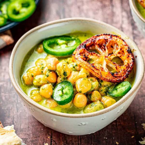 close up of two bowls of creamy pesto braised chickpeas topped with jalapeno and fried lemon slices next to a plate of sliced jalapenos.