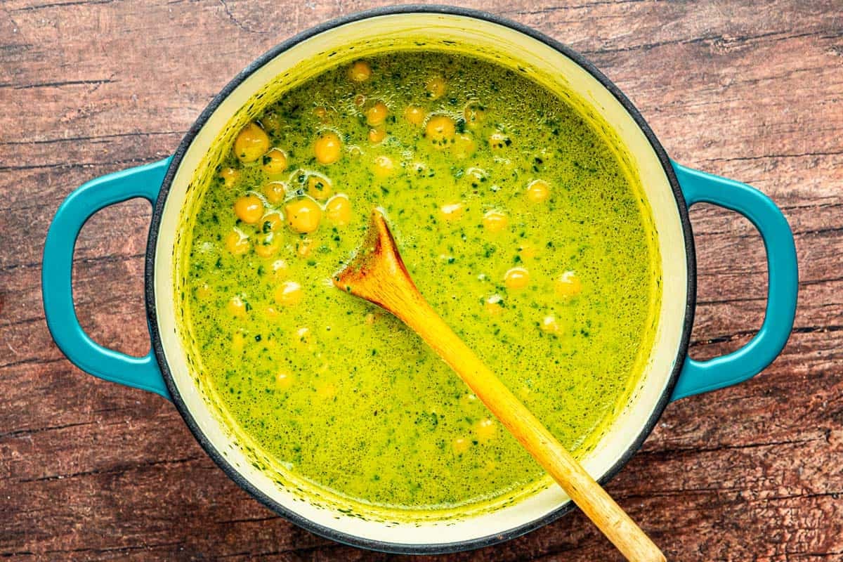 chickpeas simmering in a basil pesto sauce in a pot with a wooden spoon.