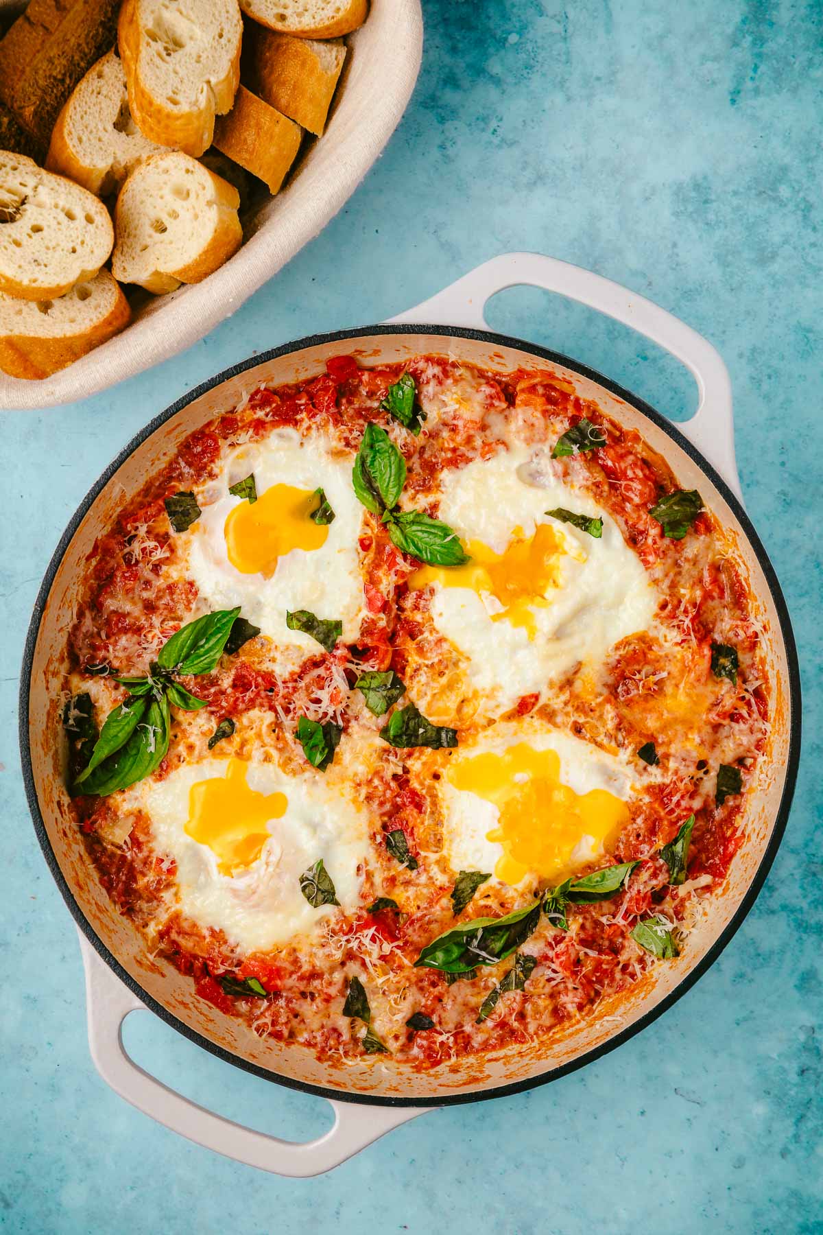 eggs in purgatory in a skillet next to a basket of sliced crusty bread.