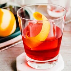 A negroni cocktail with one large ice cube and an orange twist.