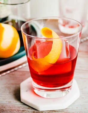 A negroni cocktail with one large ice cube and an orange twist.