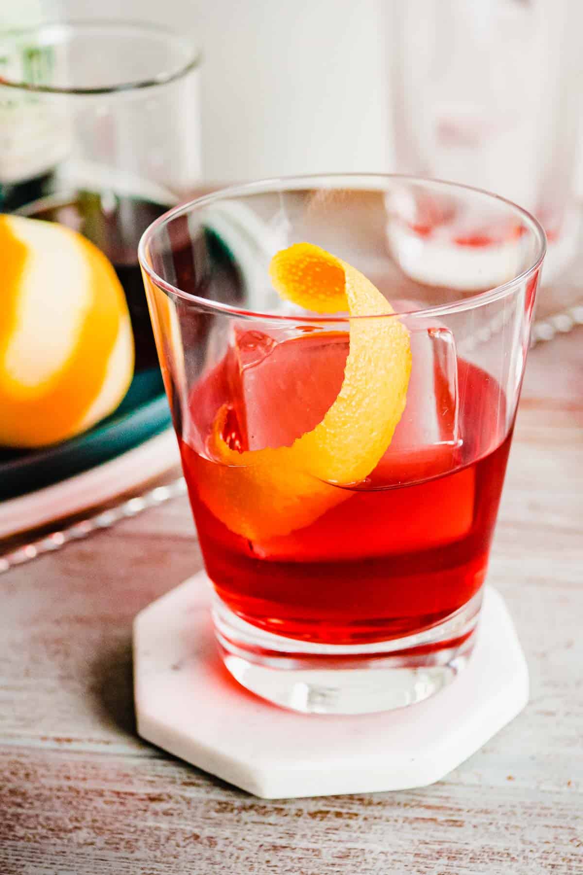 A negroni cocktail with one large ice cube and an orange twist.