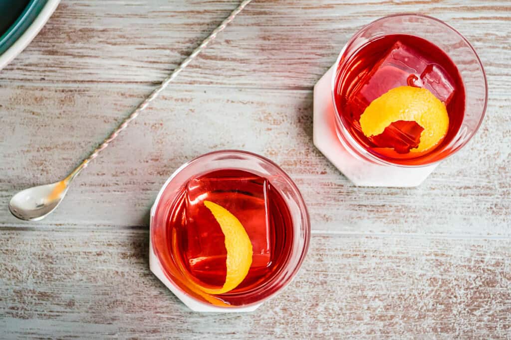 Overhead shot of two negroni cocktails with orange twists and a large cocktail stirrer on the side.