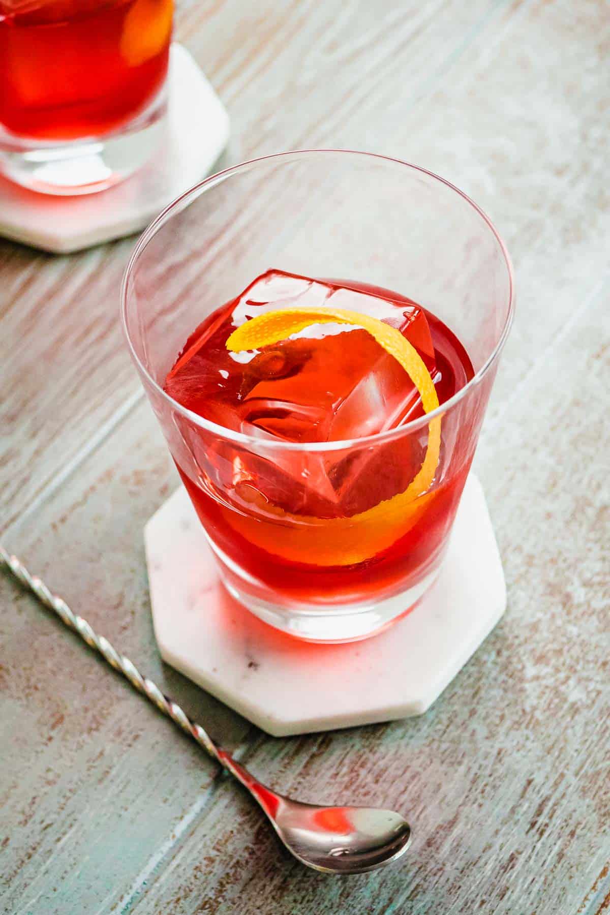 One negroni cocktail with an orange twist and a large cocktail stirrer on the side.