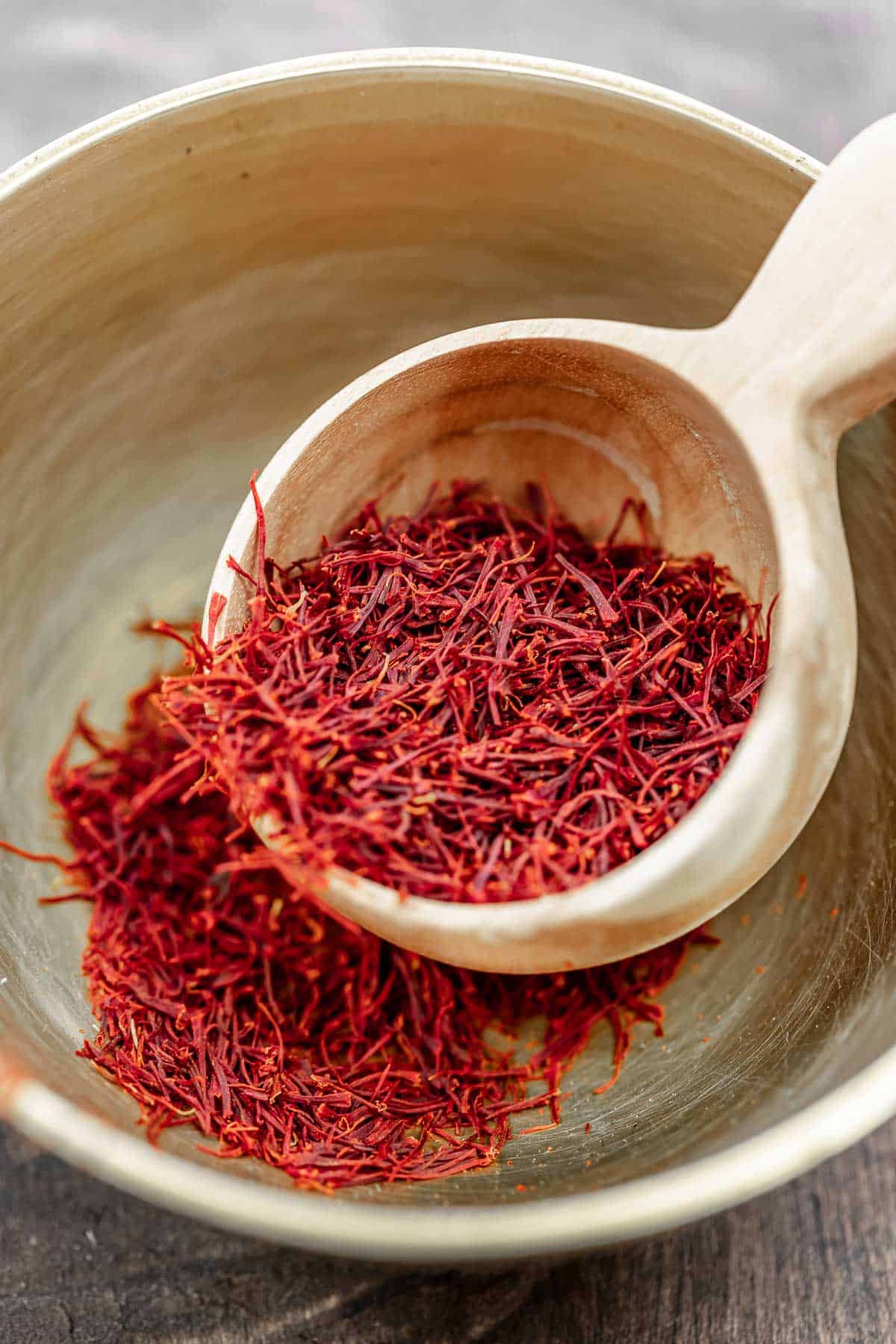 saffron threads being scooped out of a bowl with a wooden scoop.