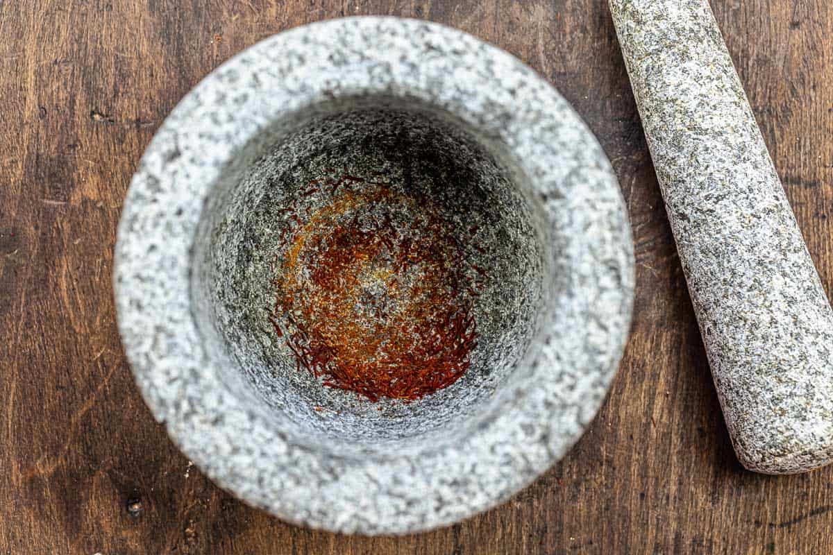 ground saffron threads in a mortar with a pestle laying next to it.