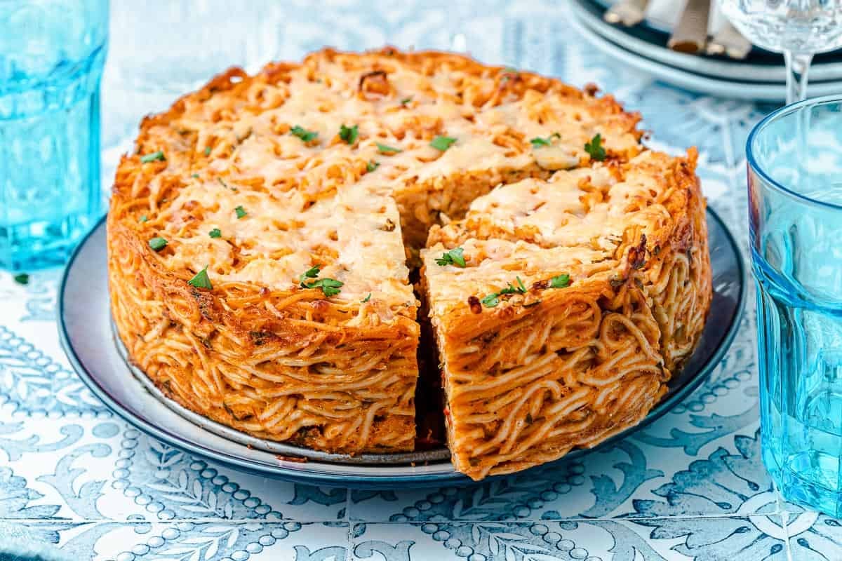 an entire spaghetti pie on a plate next to three glasses of water.