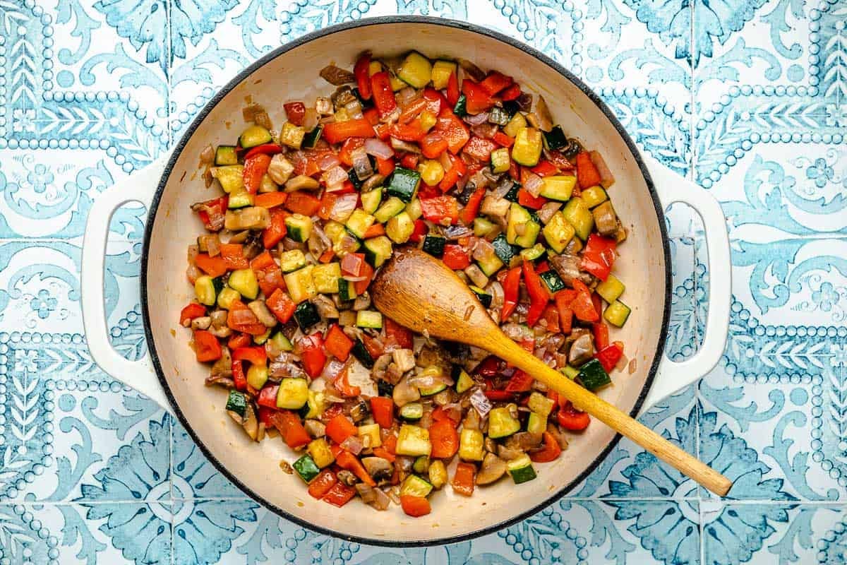 chopped, roasted vegetables sauteeing in a skillet with a wooden spoon.