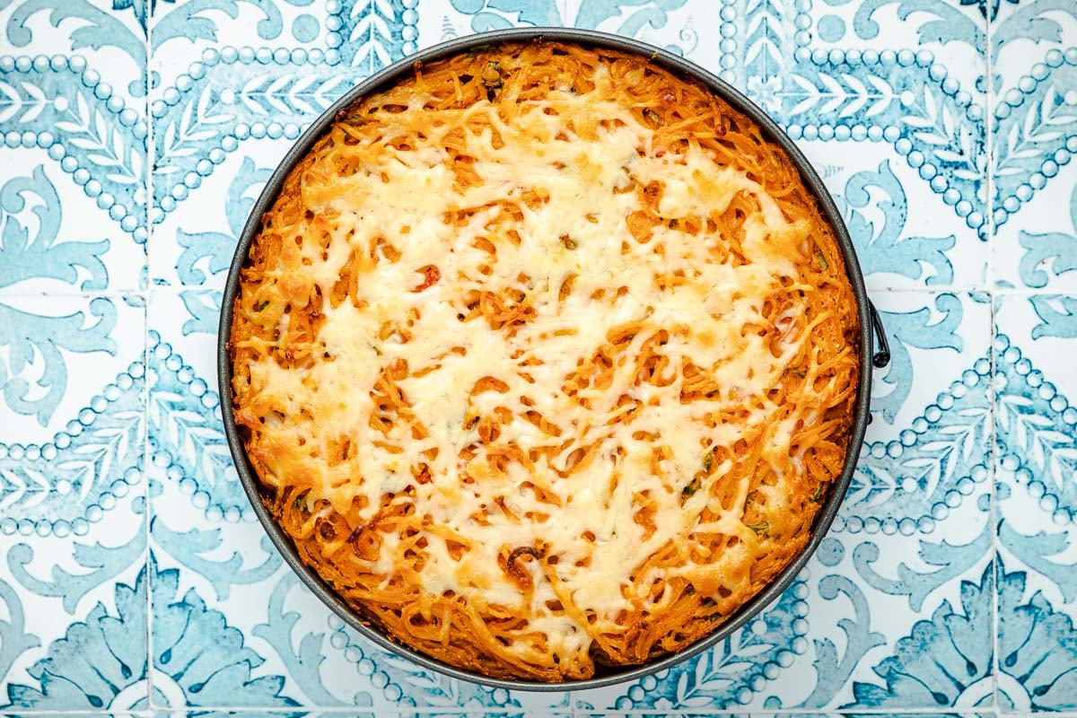 spaghetti pie topped with mozzarella cheese in a spring form pan after cooking.