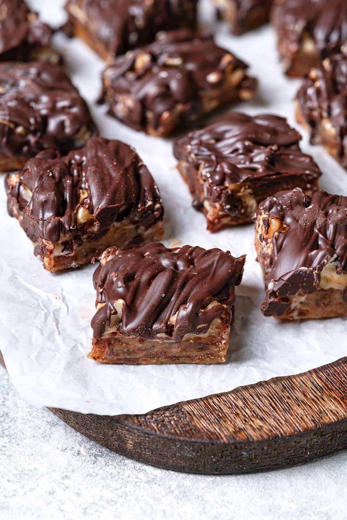 close up of several chocolate covered date bars on a parchment-lined serving tray.