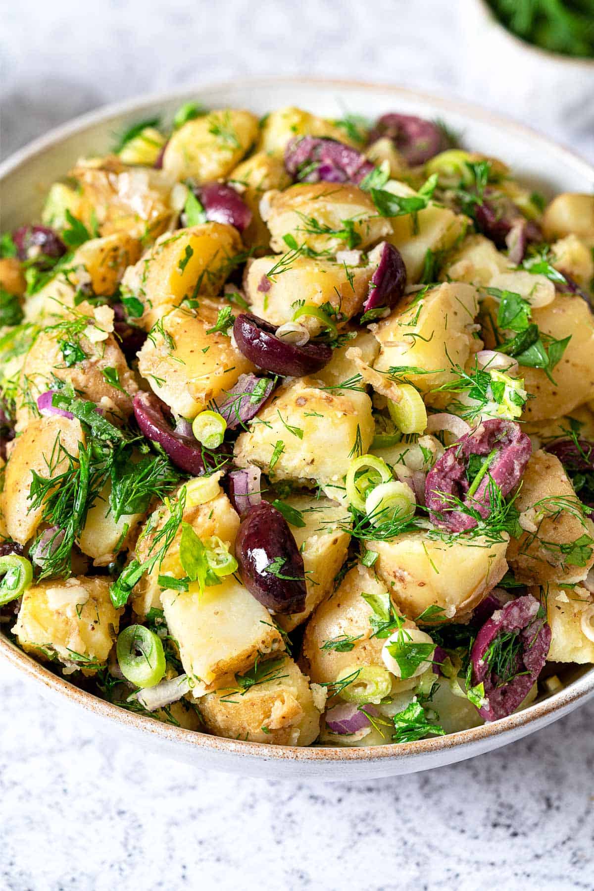 Close up of greek potato salad with olives, dill, parsley, and green onion.