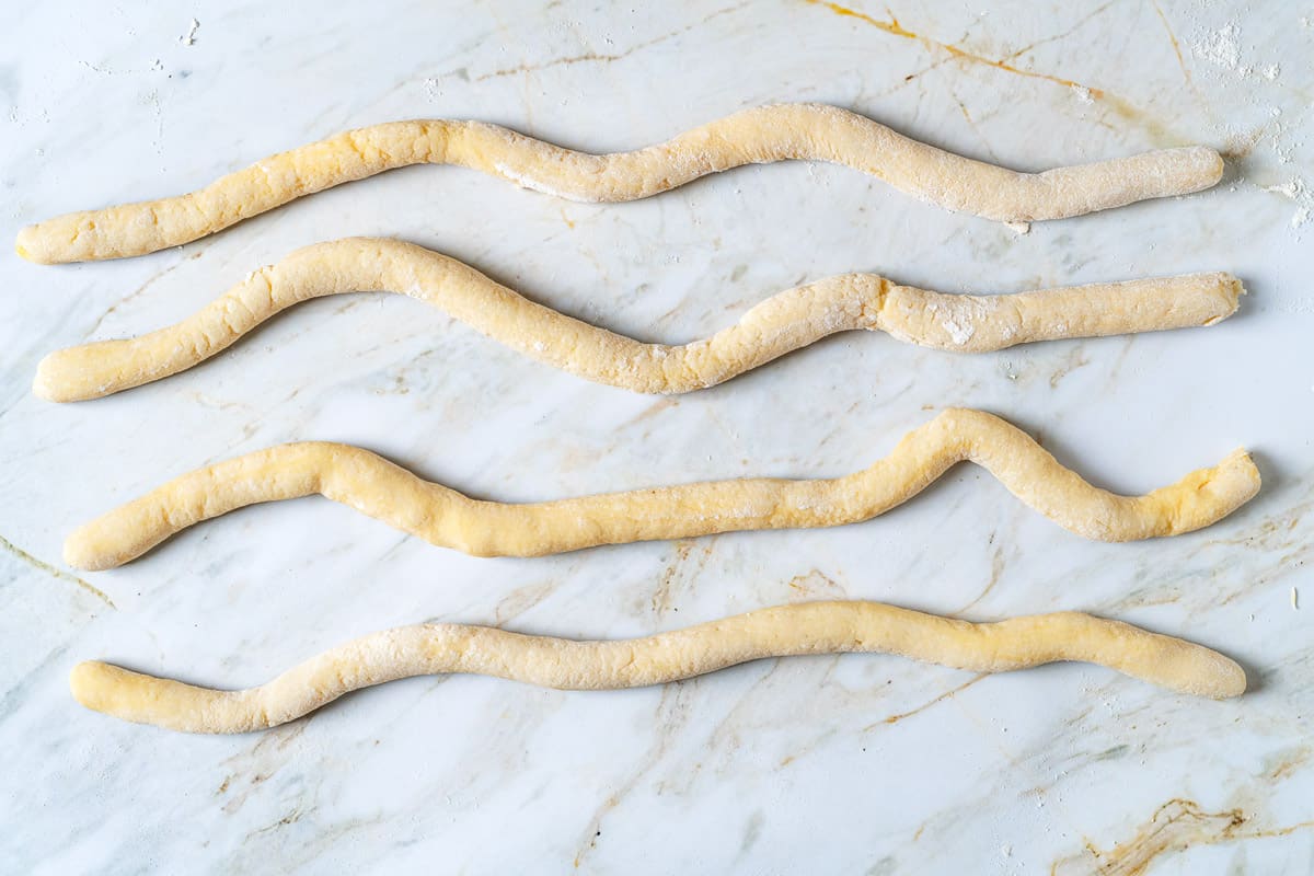 Potato gnocchi dough that has been rolled out into four snake-like pieces.