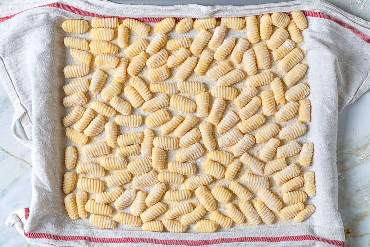 Potato gnocchi that have been shaped with ridges using a gnocchi board, resting on a towel-lined and dusted sheet tray.
