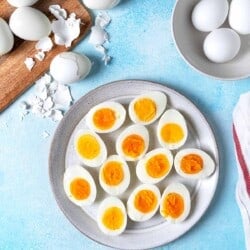 12 hard boiled egg halves on a plate next to a bowl and a wooden tray with whole hard boiled eggs.