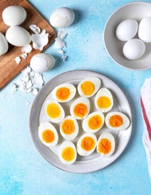 12 hard boiled egg halves on a plate next to a bowl and a wooden tray with whole hard boiled eggs.