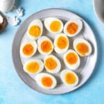 12 hard boiled egg halves on a plate next to a bowl and a wooden tray with whole hard boiled eggs.
