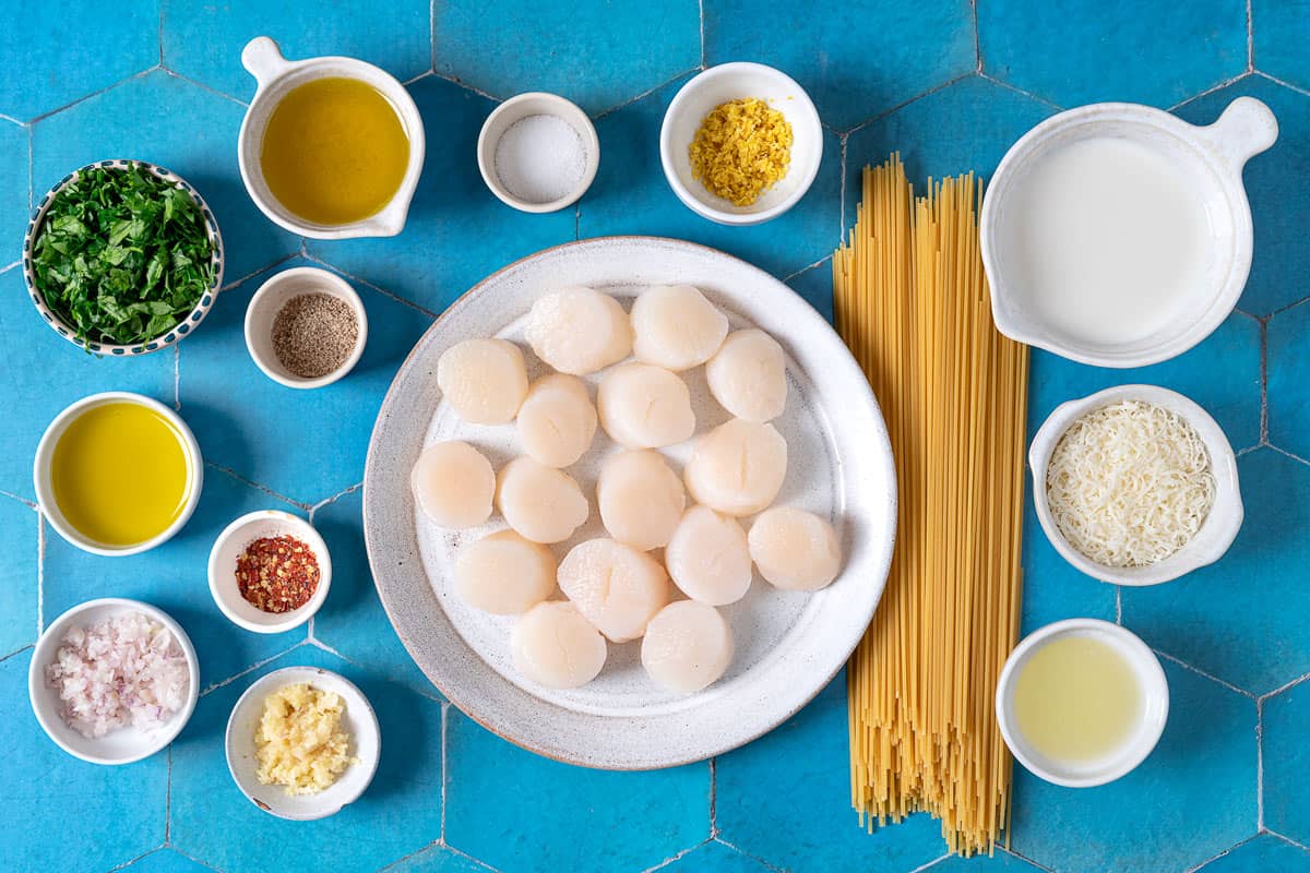 Ingredients for scallop pasta, including milk, parmesan cheese, spaghetti, olive oil, shallot, garlic, Aleppo pepper, salt, black pepper, parsley, scallops, and lemon zest.