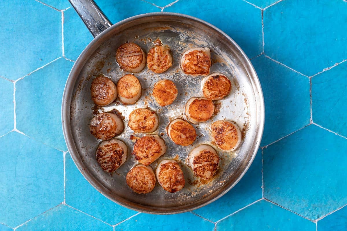Overhead shot of scallops that have been seared to golden brown in a large saucepan.