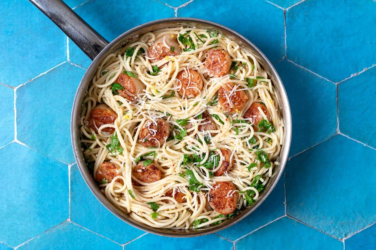 Overhead shot of a large pan of scallop pasta and a sprinkle of parmesan cheese on top.