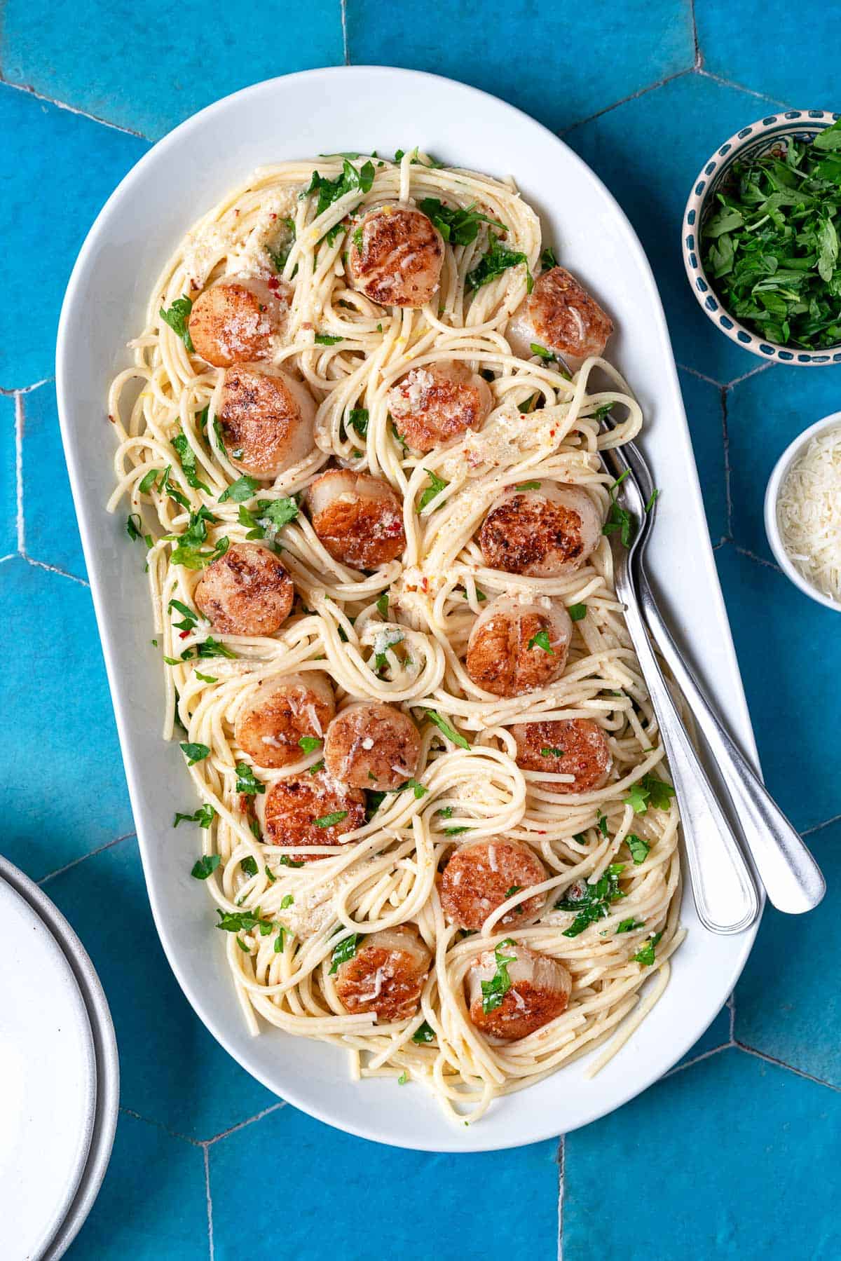 Large serving platter of scallop pasta with parsley and parmesan cheese on the side.